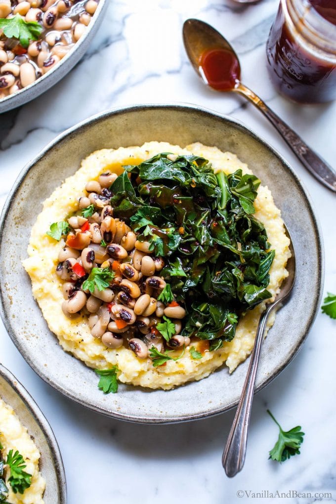 Grits and greens with black eyed peas with grits in a bowl with a spoon.