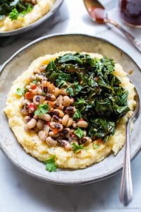 Grits and greens with black eyed peas with grits in a bowl with a spoon.