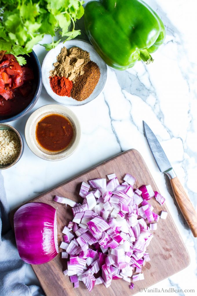 Ingredients for tofu tacos, with a red onion being chopped on a cutting board.