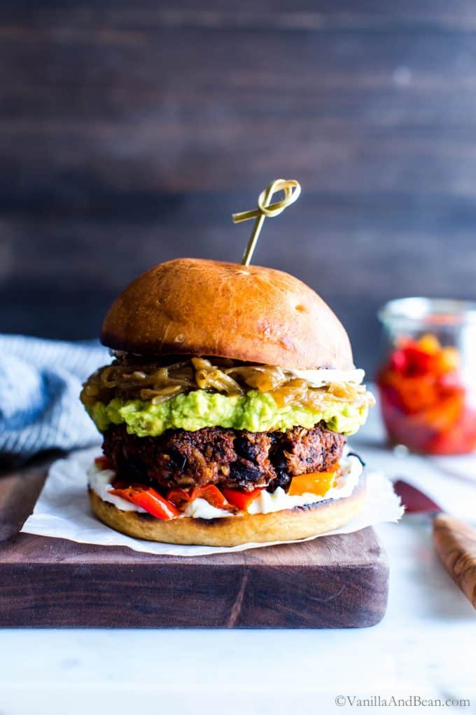Vegan Black bean Walnut burgers on a board topped with saucy onions and guacamole.
