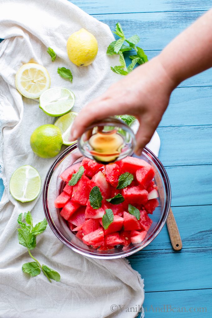 Pouring maple syrup into watermelon and mint in a bowl. 