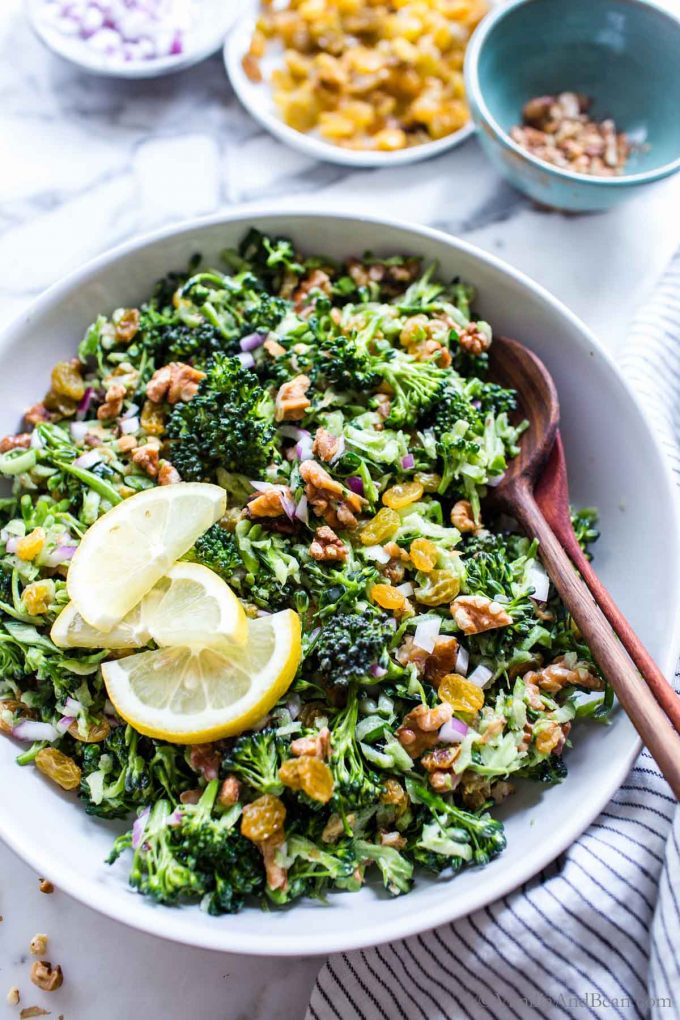 Broccolini Slaw in a bowl with two spoons garnished with lemons.