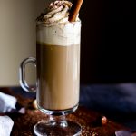 Boozy Coffee in a tall coffee glass topped with whipped cream and a cinnamon stick.
