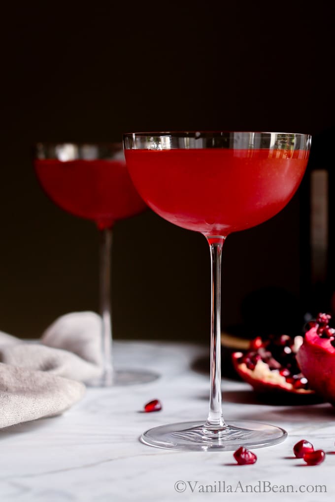 A pear and orange liqueur, pomegranate and orange juice cocktail. Winter Punch in two coupe glasses. 