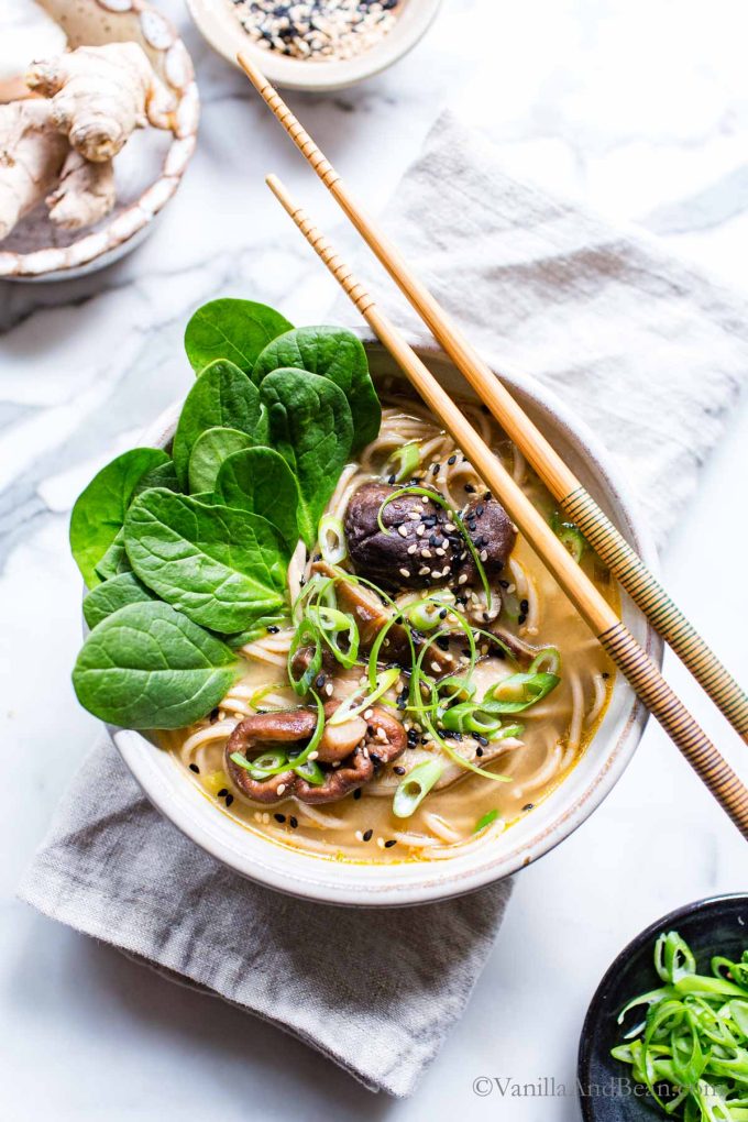1. vegetarian and vegan ramen in a bowl with chop sticks resting on the side, garnished with onions, spinach and sesame seeds.