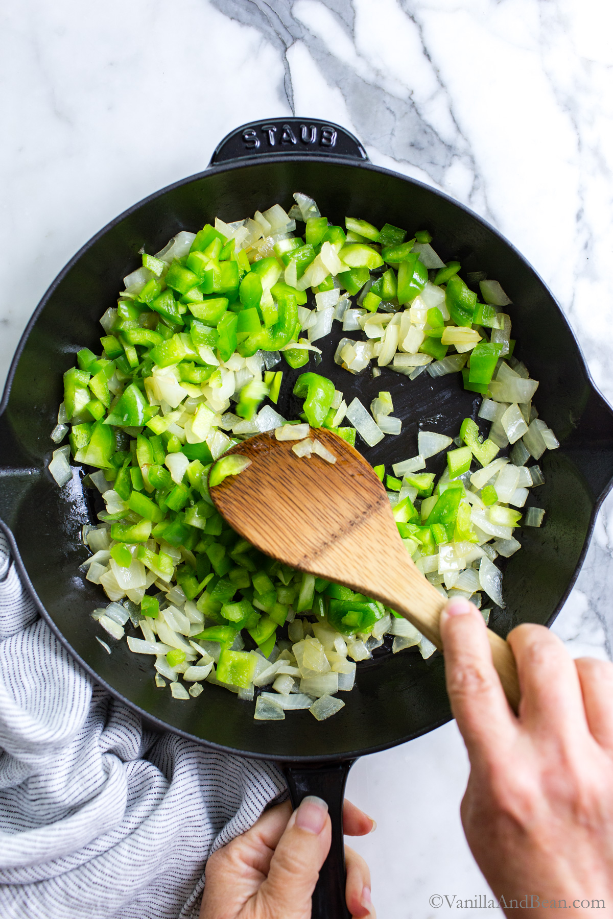 Onions and bell pepper in a skillet being stirred.
