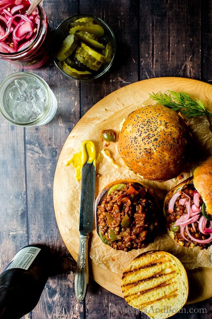 An overhead image of Tangy Lentil Sloppy Joes sandwiches, served with pickles and pickled onions on the side. 
