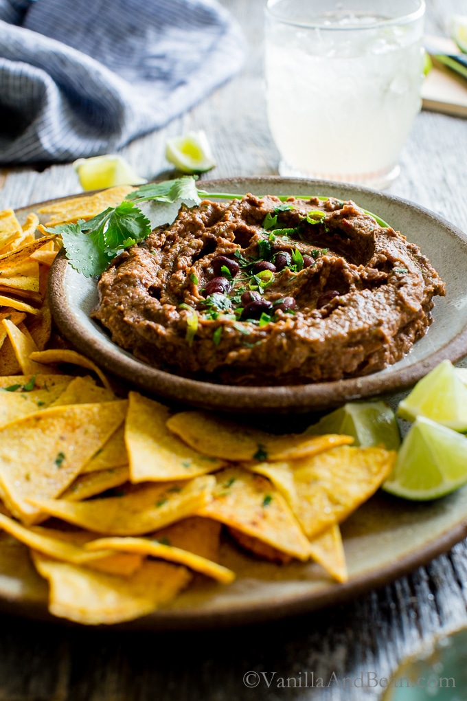 Chipotle Black Bean Dip on a table shared on a plate with tortilla chips, drinks with lime and salt.