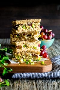 Smashed Chickpea Salad with Pecans and Grapes tea sandwiches stacked up on a cutting board.