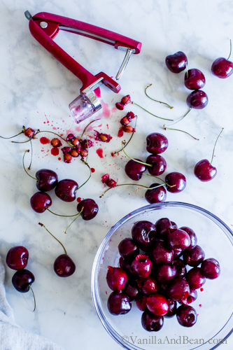Pitting bing cherries with a cherry pitter and a bowl full of pitted cherries. 