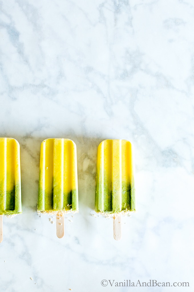 Three Matcha-Mango Coconut Popsicles on a marble counter. 
