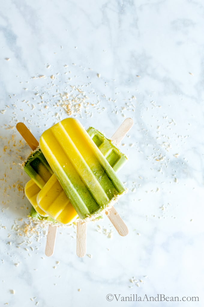 Matcha-Mango Coconut Popsicles stacked up on a marble counter. 