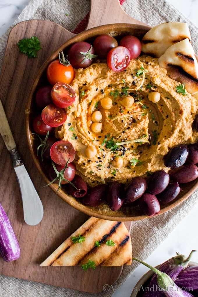Roasted eggplant hummus on a cutting board shared with Naan, olives and tomatoes.