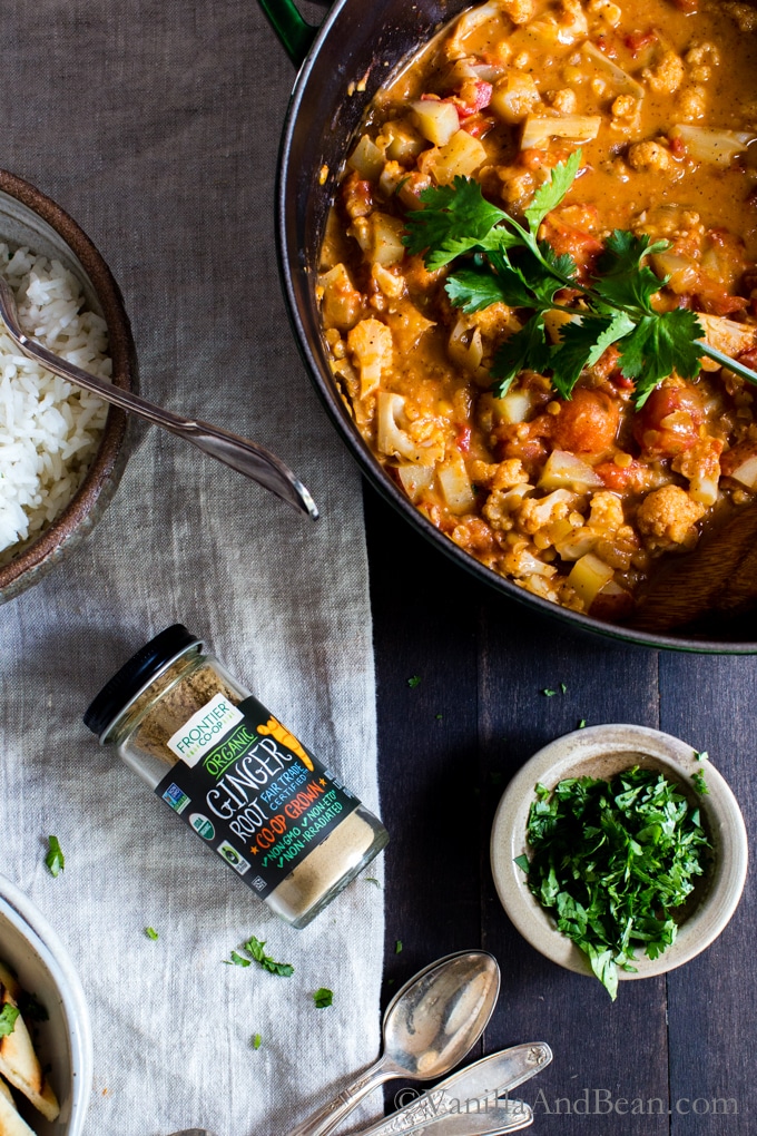 Overhead shot of Cauliflower-Potato Red Lentil Curry with a jar of ginger ground spice, rice and cilantro. 