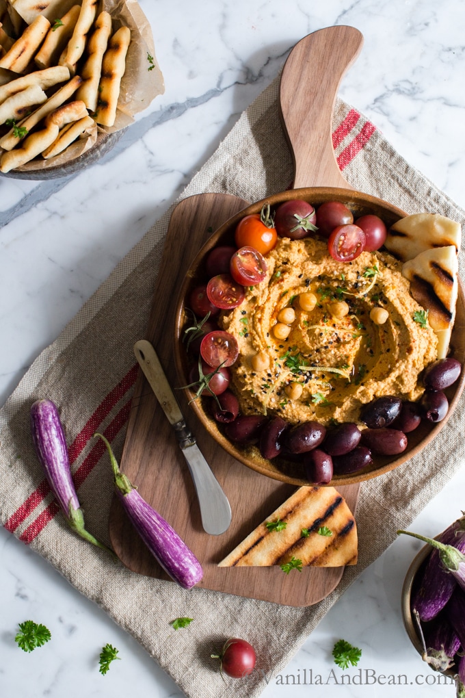 Roasted eggplant hummus on a cutting board shared with Naan, olives and tomatoes. 