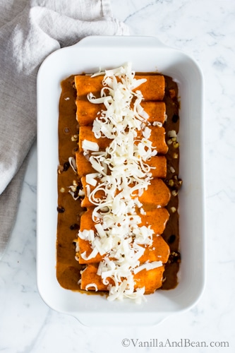 Sweet Potato Wrapped Black Bean Enchiladas in a casserole topped with cheese, ready to be baked. 