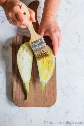 Brushing olive oil on the eggplant on a cutting board. 