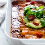 Sweet Potato Wrapped Black Bean Enchiladas in a casserole dish topped with avocado and cilantro ready for sharing.