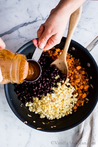 Adding the Enchilada sauce to the pan with corn, black beans and sweet potatoes. 