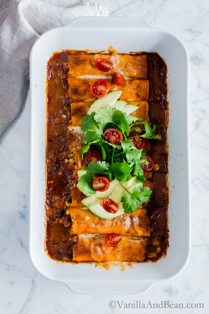 Sweet Potato Wrapped Black Bean Enchiladas in a casserole dish topped with avocado and cilantro ready for sharing.