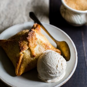 Tender pastry wrapped around half an apple stuffed with a mix of brown sugar, cinnamon, butter and cranberries on a plate with a scoop of ice cream.