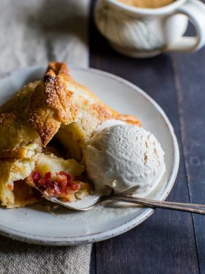 Tender pastry wrapped around half an apple stuffed with a mix of brown sugar, cinnamon, butter and cranberries on a plate with a scoop of ice cream.