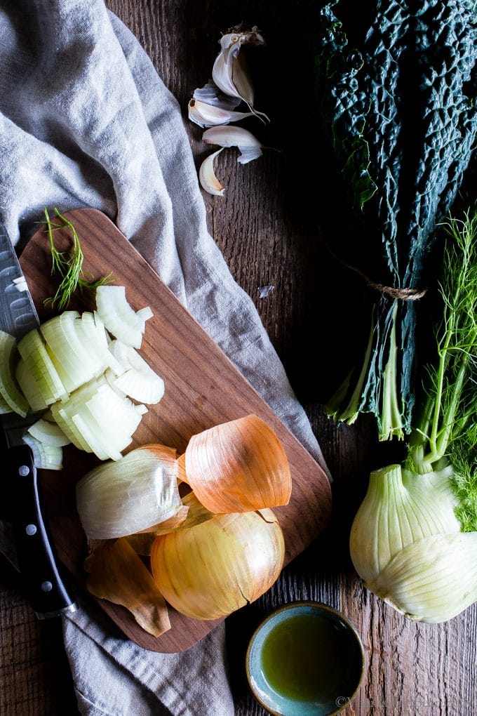 Slicing onion on a cutting board with kale and fennel on the side. 