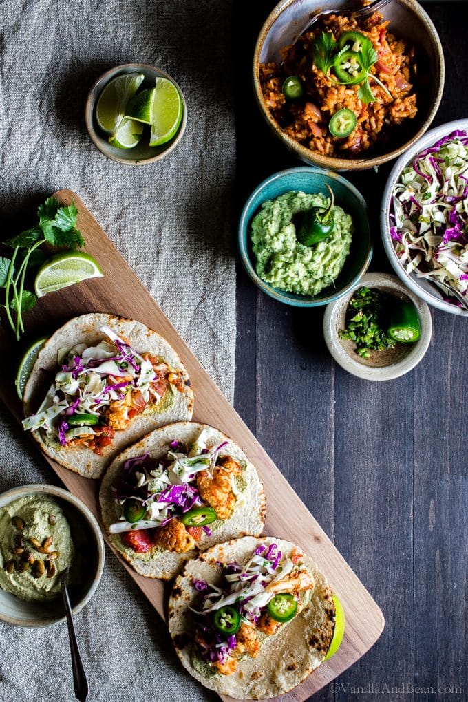 Roasted cauliflower tinga tacos with Spanish rice, guacamole, peppers and slaw on a board. 