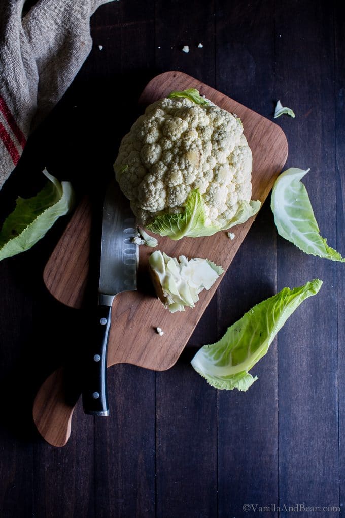 Cauliflower and a knife on a cutting board. 