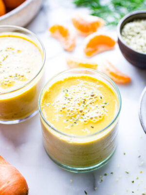 Two glasses of citrus ginger carrot smoothie on a table sprinkled with hemp hearts.