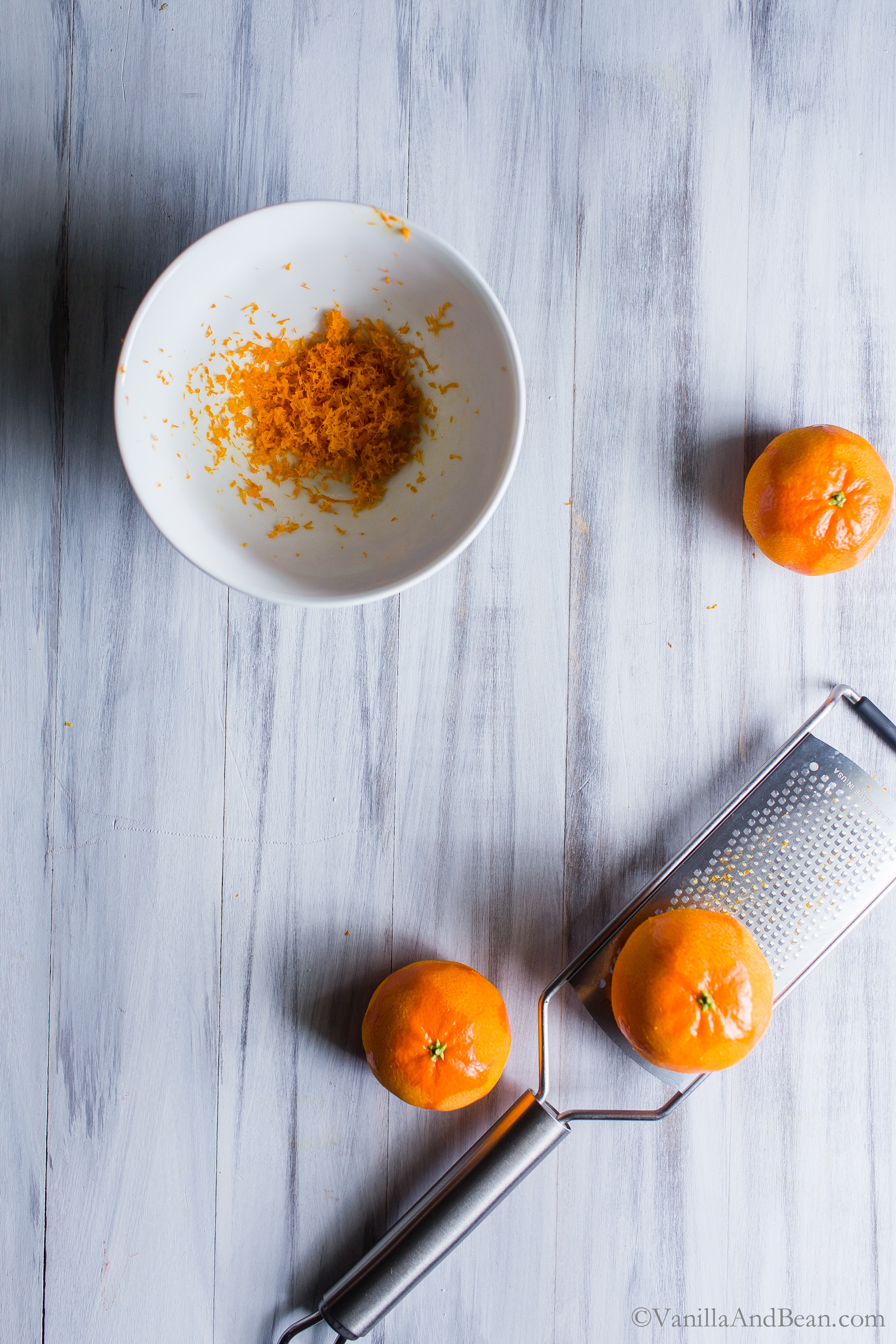 Zesting oranges and collecting zest in a bowl. 
