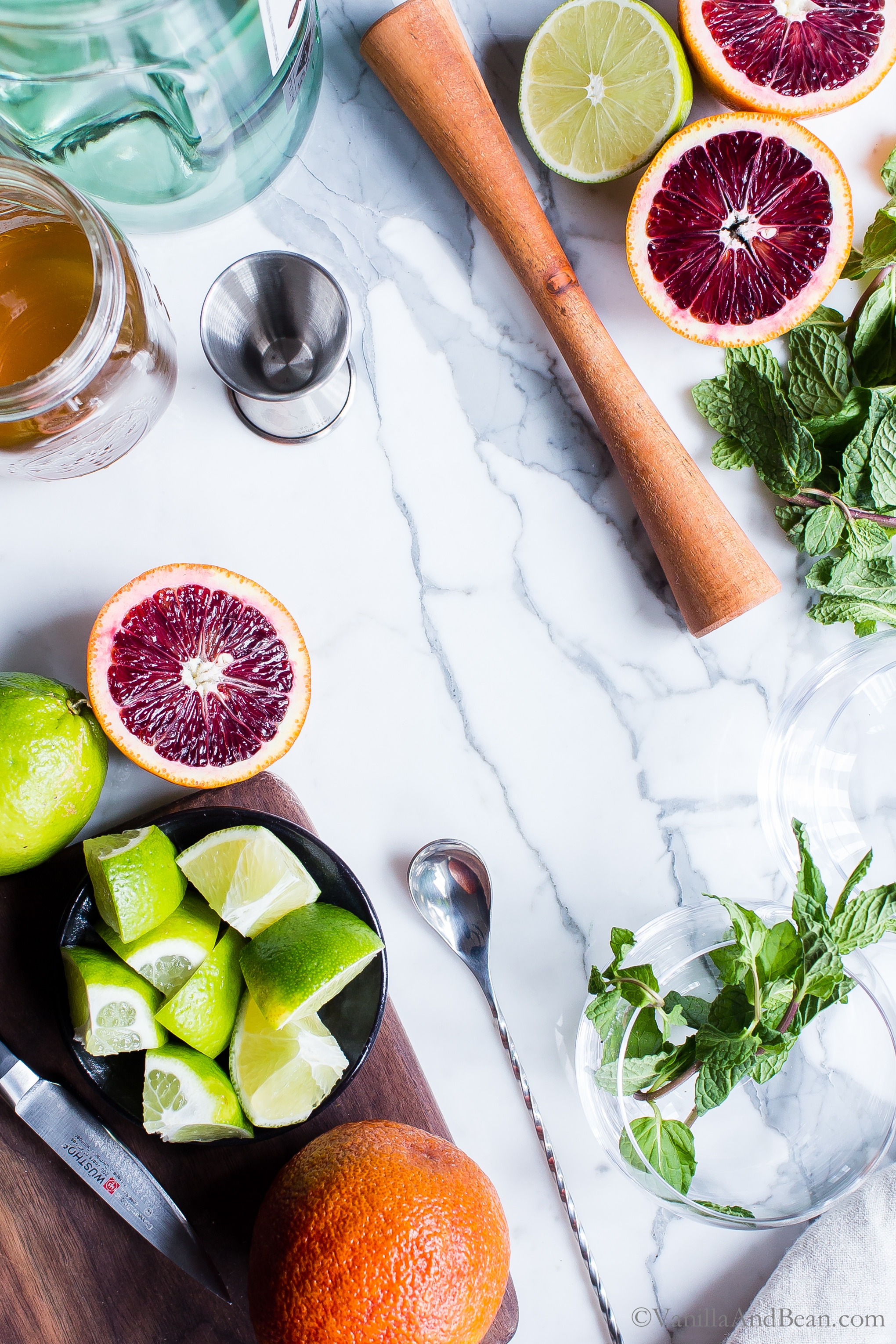 Overhead shot of ingredients for Blood Orange Mojitos with a muddler, spoon and cocktail glasses. 