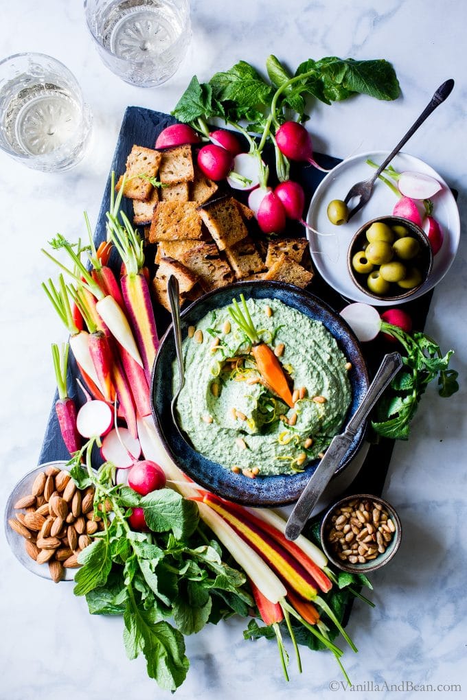 Overhead shot of Pesto-Spinach Whipped Ricotta Dip shared with veggies, crackers, nuts and olives.