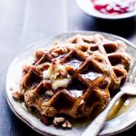 Banana-Pecan Oat Waffles drizzled with maple syrup on a plate ready for sharing.