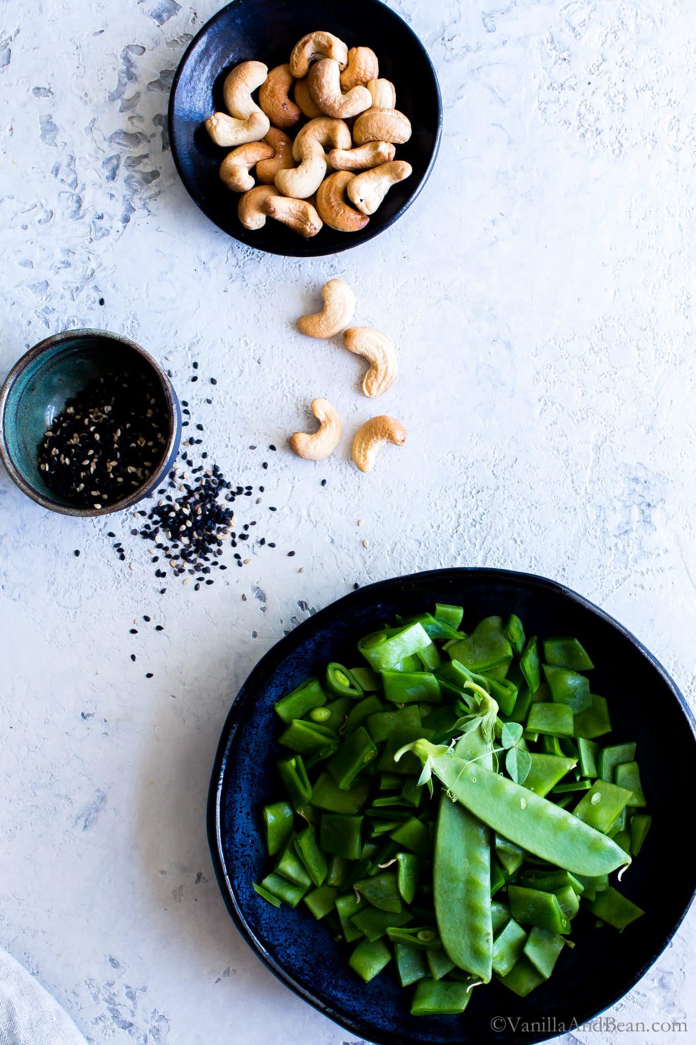 Ingredient bowls of sliced snow peas, cashews and sesame seeds. 