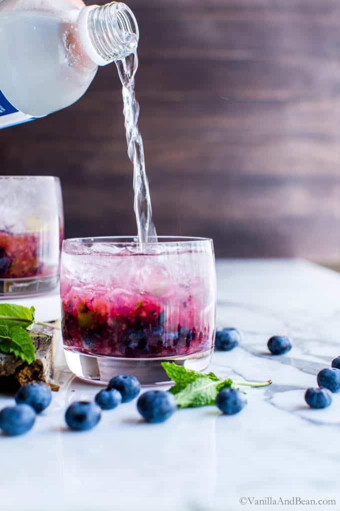 Pouring club soda into blueberry mojitos. 