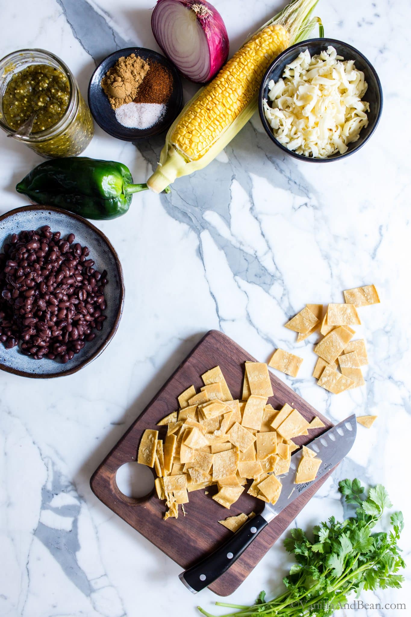 Ingredients for Skillet Black Bean Vegetarian Enchiladas Verde and sliced corn tortillas on a cutting board. 