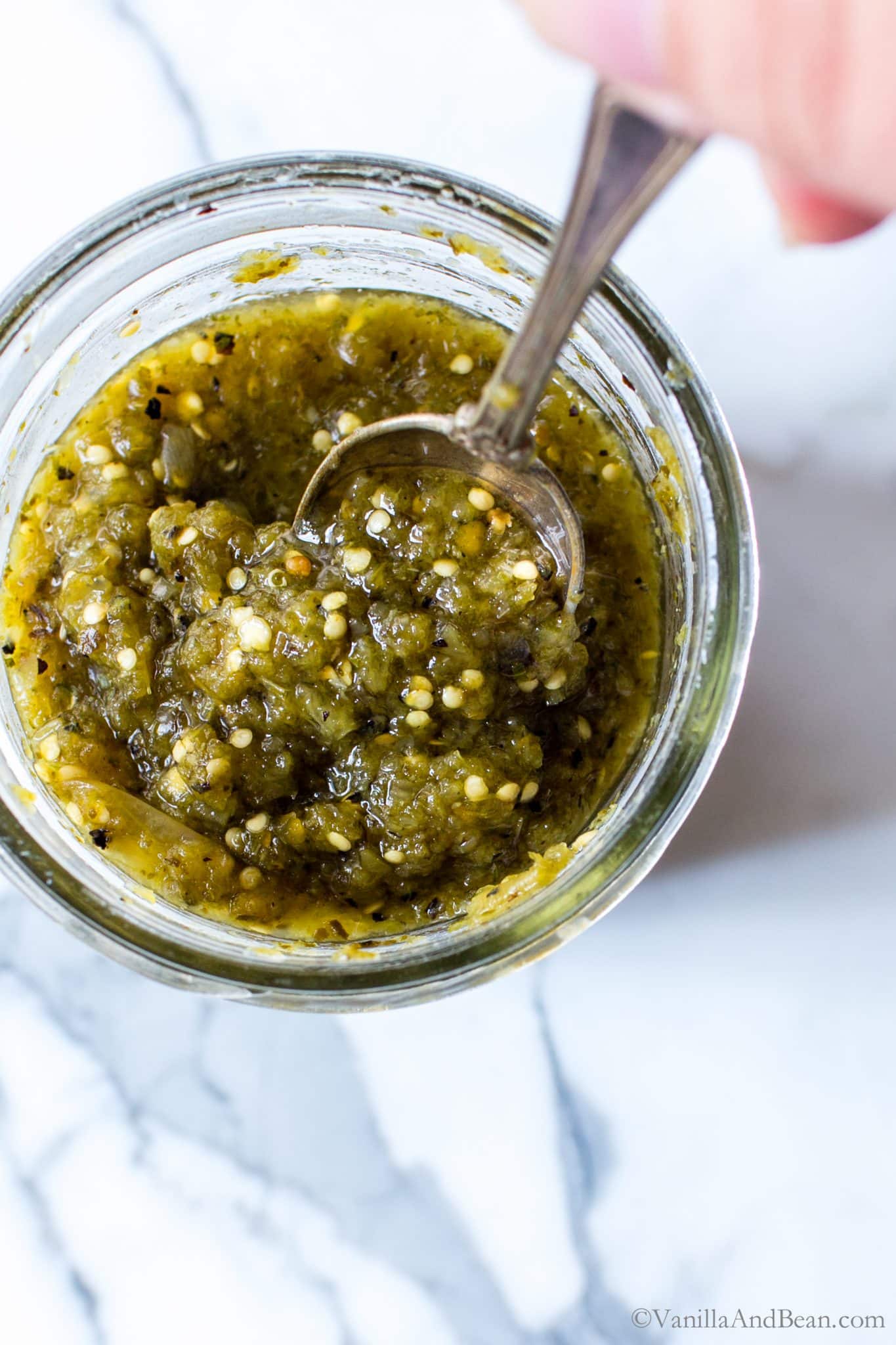 Homemade tomatillo salsa in a jar with a spoon in it. 