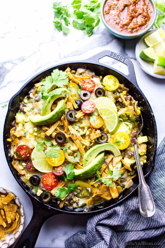 Easy Skillet black bean enchiladas verde garnished with avocado, cilantro and tomatoes in a skillet ready for sharing.