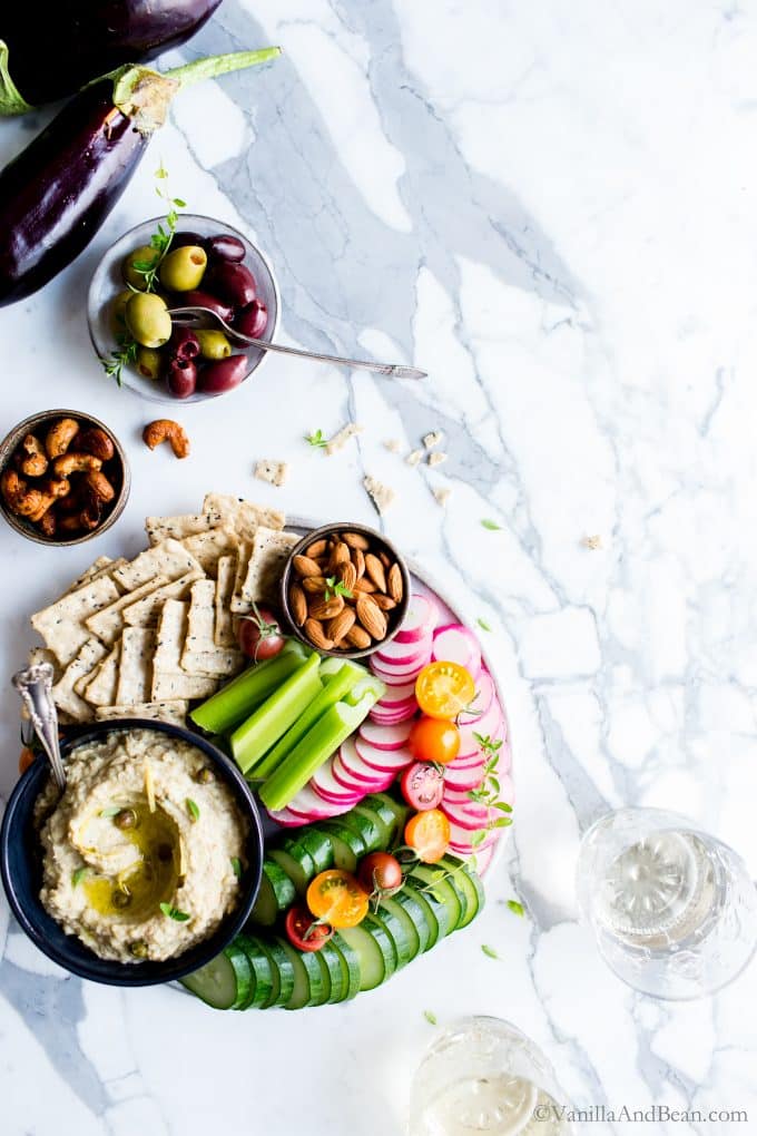 Overhead shot of Roasted Eggplant Artichoke White Bean Dip shared with fresh veggies, olives and nuts. 