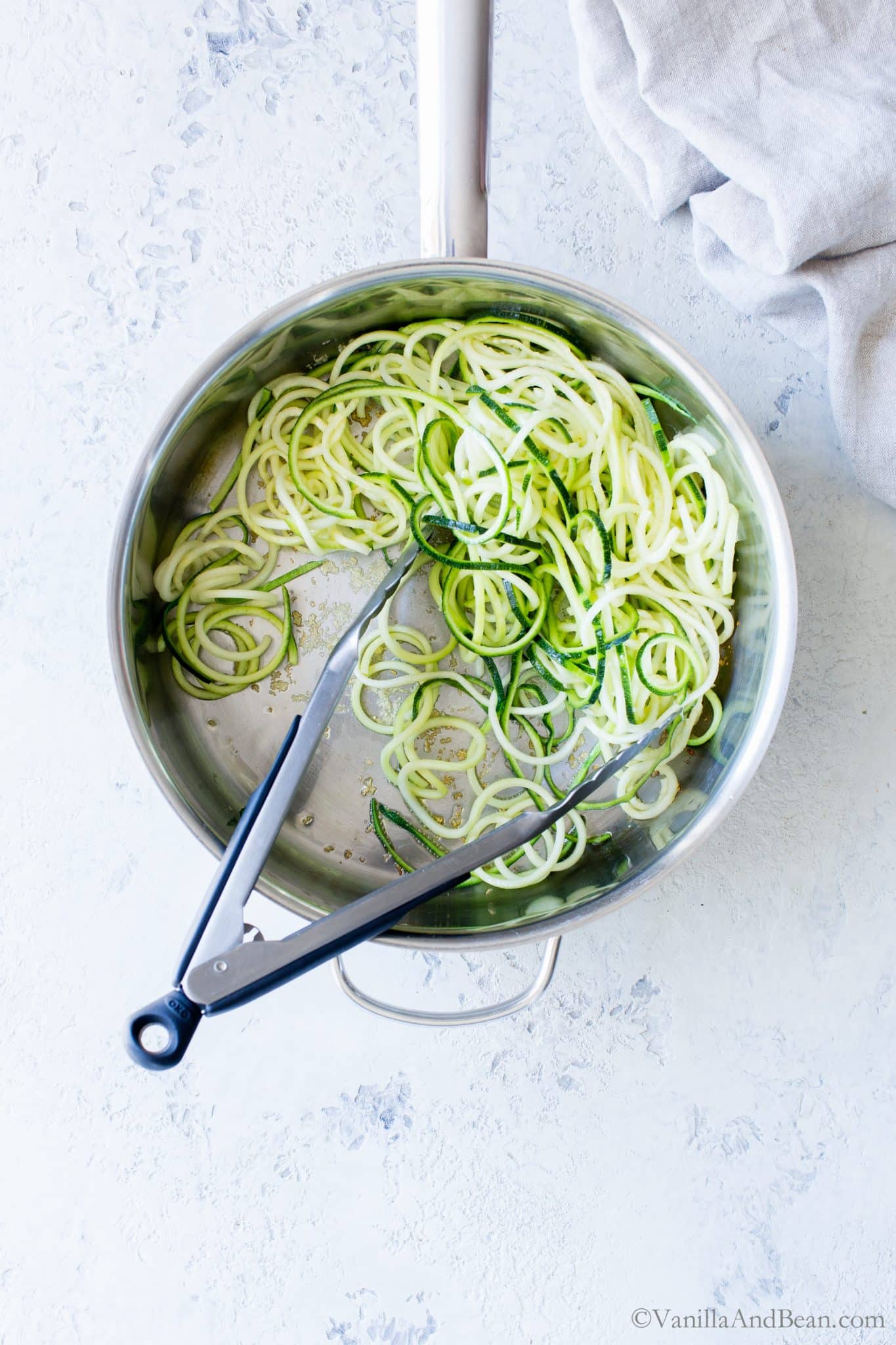 Zucchini Noodles in a skillet, tossed with tongs. 