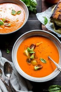 Roasted Red pepper and tomato soup in serving bowls, garnished with tomatoes and basil.