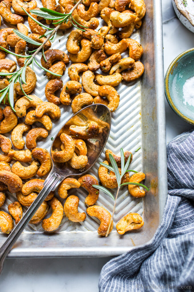 Rosemary Roasted Cashews on a sheet pan with a spoon holding a few cashews.