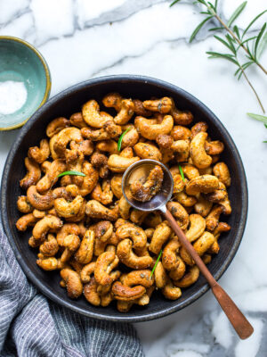 Roasted rosemary cashews in a serving bowl garnished with rosemary leaves.