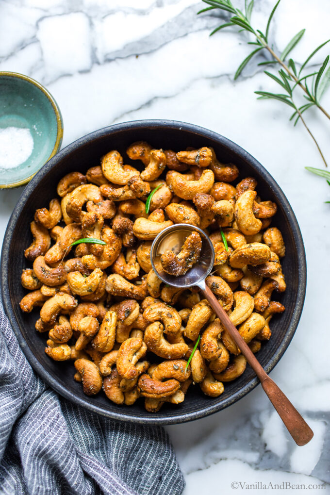 Roasted rosemary cashews in a serving bowl garnished with rosemary leaves.