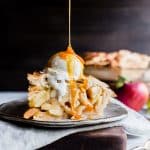 Apple Pie with ice cream on top and a drizzle of caramel sauce on a plate.