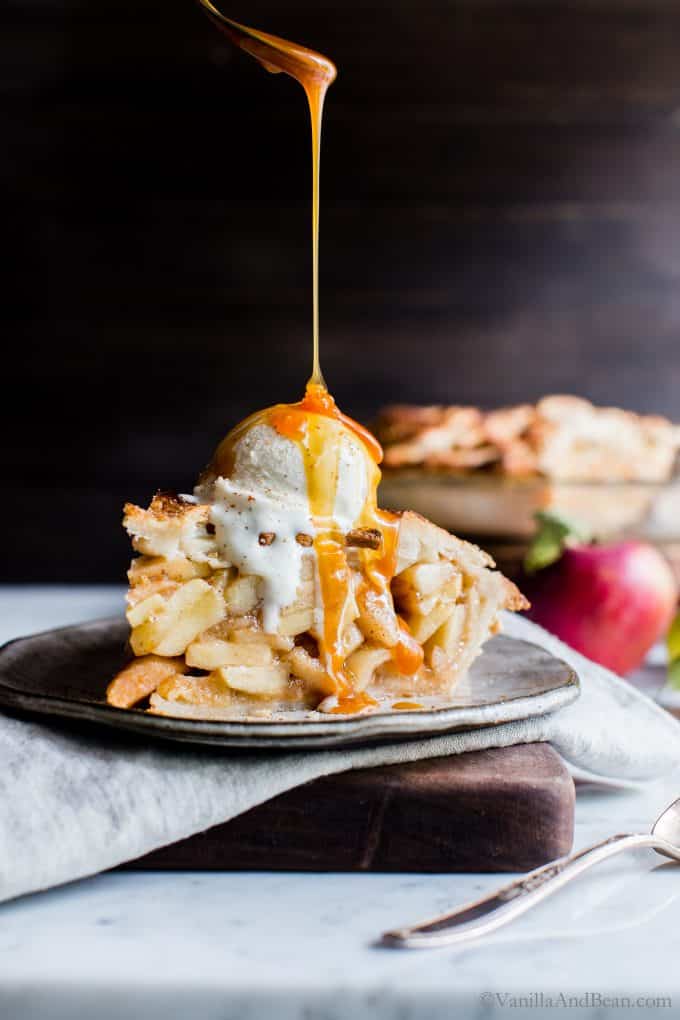 Apple Pie with ice cream on top and a drizzle of caramel sauce on a plate. 
