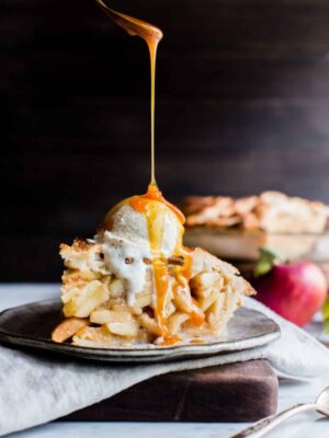 Apple Pie with ice cream on top and a drizzle of caramel sauce on a plate.