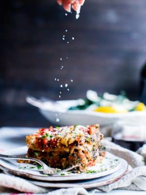 Spinach and mushroom lasagna with Parmesan being sprinkled over the top.