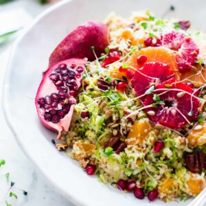 Shaved Brussels Sprouts Citrus Quinoa Salad with a snappy Honey-Orange Dijon Vinaigrette in a serving bowl garnished with pomegranates and orange slices.